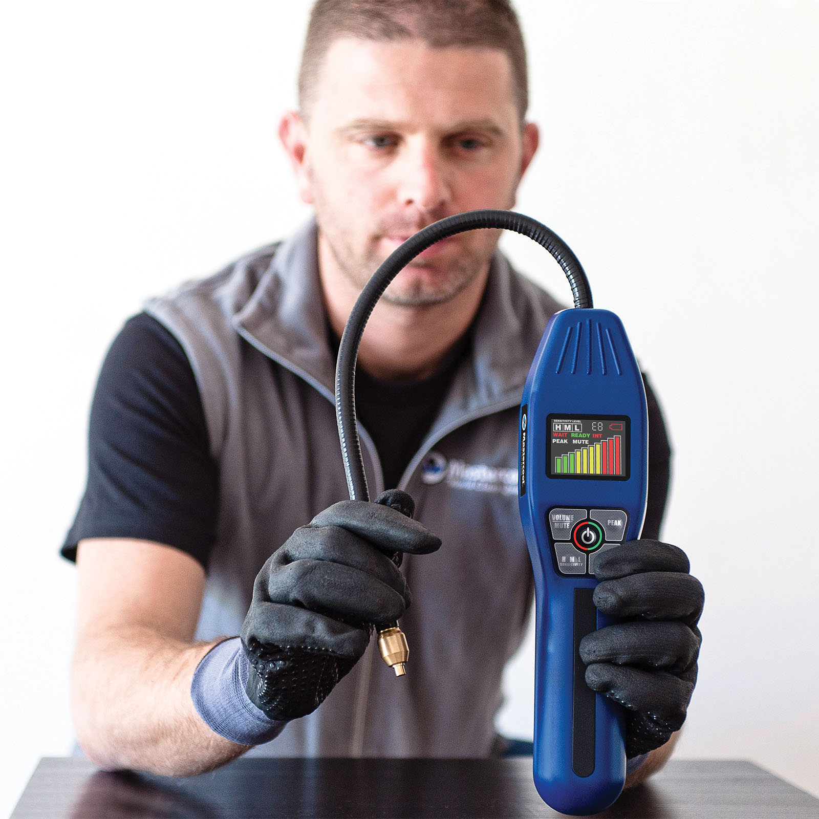 Man holding a blue diagnostic tool with a digital display, wearing gloves.