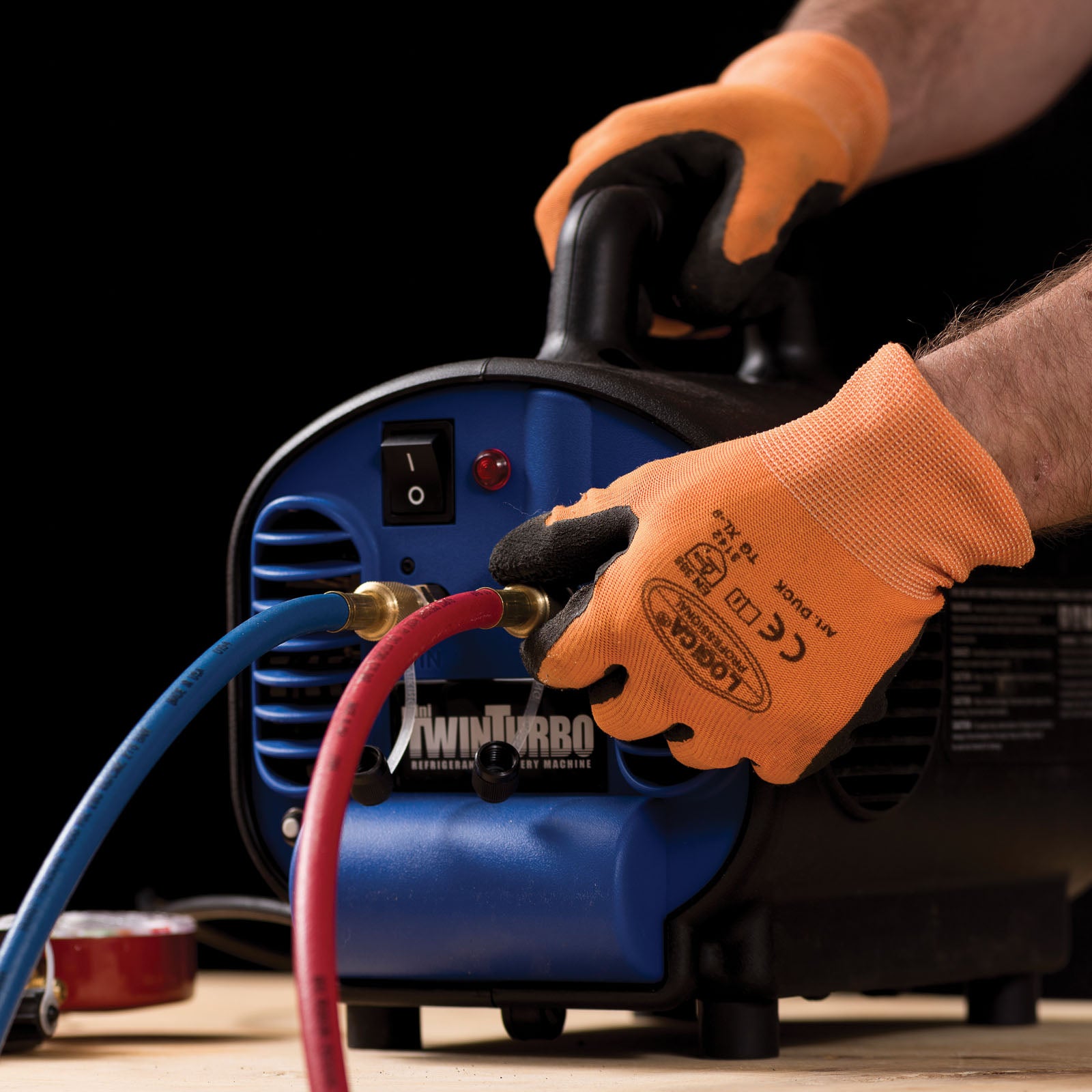 Person wearing orange gloves connecting a hose to a blue and black portable power washer.