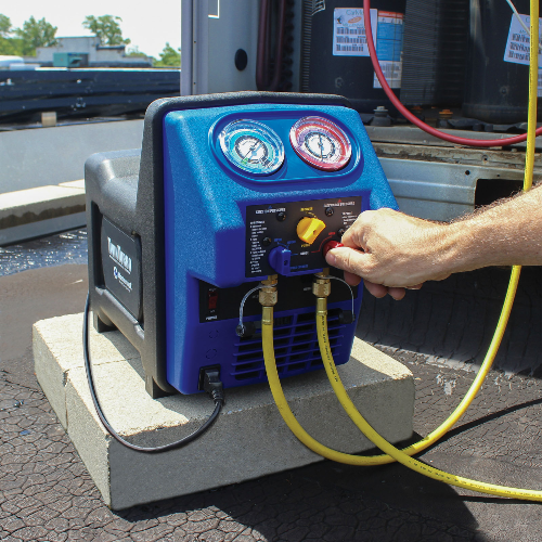 Hand operating a blue and black air compressor with hoses attached on a vehicle.