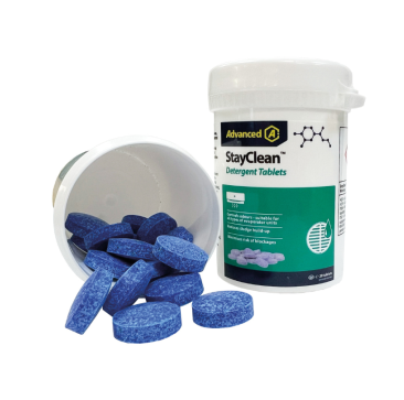 A white plastic bottle labelled "Advanced A StayClean Detergent Tablets" with a blue cap contains small, round blue tablets for air conditioning drain maintenance. Several blue tablets spill out onto a white surface, and green accents on the label highlig