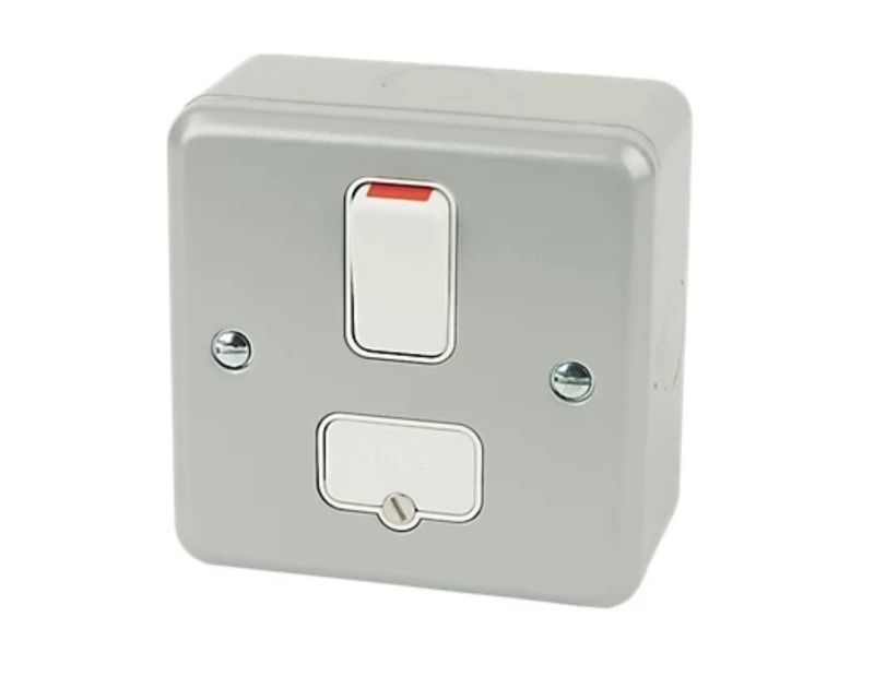 A grey metal-clad switched spur with a 13 Amp rating, featuring a white toggle switch with a red indicator and a fuse compartment labelled "FUSE" below it. The unit has rounded edges and four mounting screws, one at each corner.