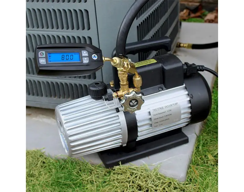 Mastercool 98063-BT Digital Vacuum Gauge connected to a two-stage vacuum pump, attached to an HVAC unit outdoors. The gauge displays '800 Micron' on its LCD screen. The setup includes brass fittings and black hoses, with the pump labelled 'Two Stage Vacuu