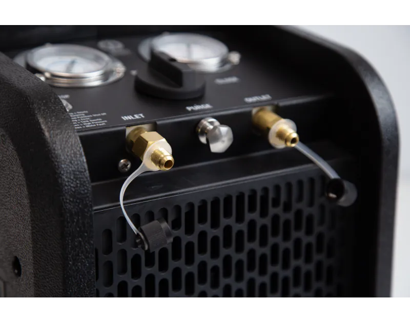 Close-up of the JAVAC Velo-X Twin Cylinder Recovery Unit Pro control panel, featuring dual pressure gauges, a selector knob with 'Close,' 'Purge,' and 'Recover' settings, brass inlet and outlet fittings with hoses, and a perforated front for ventilation.