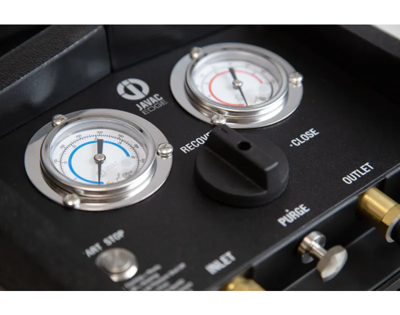 A close-up view of the control panel of a black JAVAC Edge Velo-X Recovery Unit featuring two pressure gauges labelled "INLET" on the left and "OUTLET" on the right. The gauges display pressure readings in bar and psi, with the inlet gauge showing a blue 