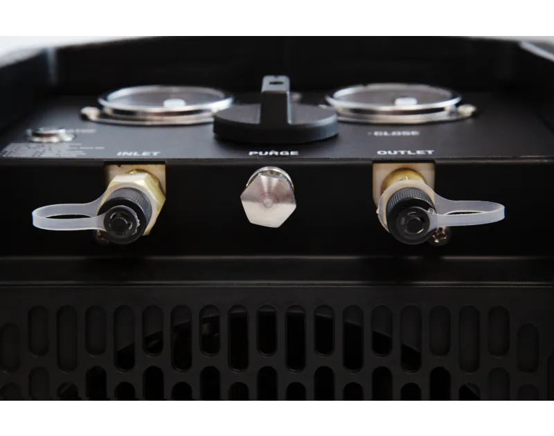 A close-up view of the front panel of a black JAVAC Edge Velo-X Recovery Unit featuring two pressure gauges labelled "INLET" on the left and "OUTLET" on the right. Each gauge has a brass fitting with a black cap and a clear plastic cover attached. In the 